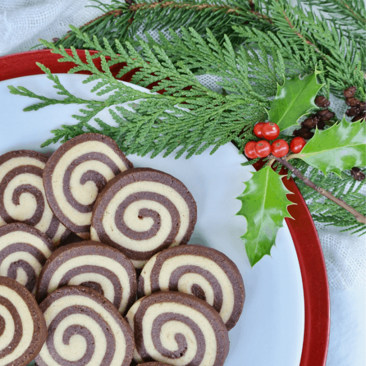 A festive, holly garnished plate showing the tight spiral of these black and white pinwheel cookies.