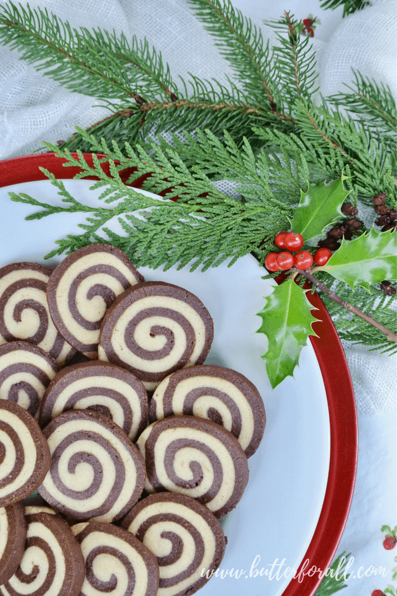 A festive, holly garnished plate showing the tight spiral of these black and white pinwheel cookies.