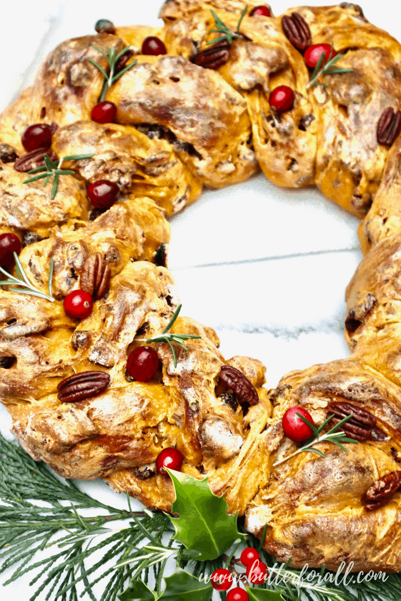 A festive, bright orange sourdough wreath with cranberry, pecan, and rosemary garnish.