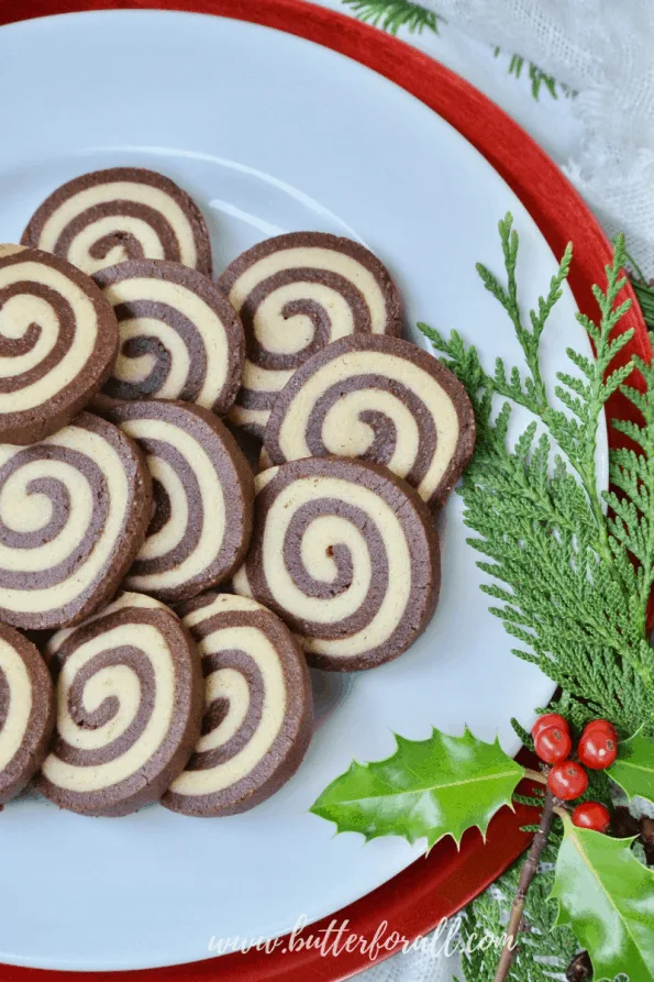 A festive, holly-garnished plate showing the tight spiral of these black and white pinwheel cookies.