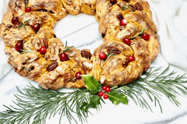 A festive, bright orange sourdough wreath with cranberry, pecan, and rosemary garnish. 