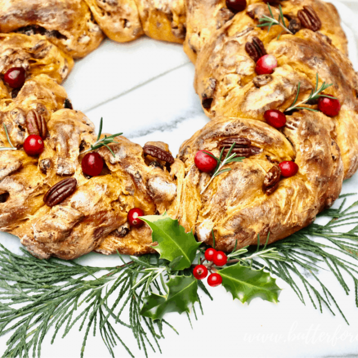 A festive, bright orange sourdough wreath with cranberry, pecan, and rosemary garnish.
