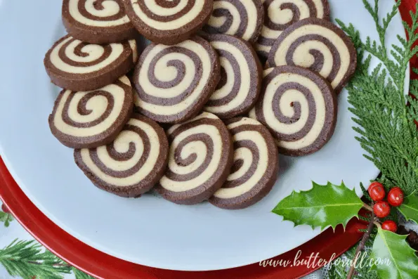 A festive, holly-garnished plate showing the tight spiral of these black and white pinwheel cookies.
