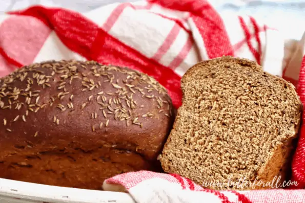 A basket of dark colored sourdough rye bread with caraway seeds on top.