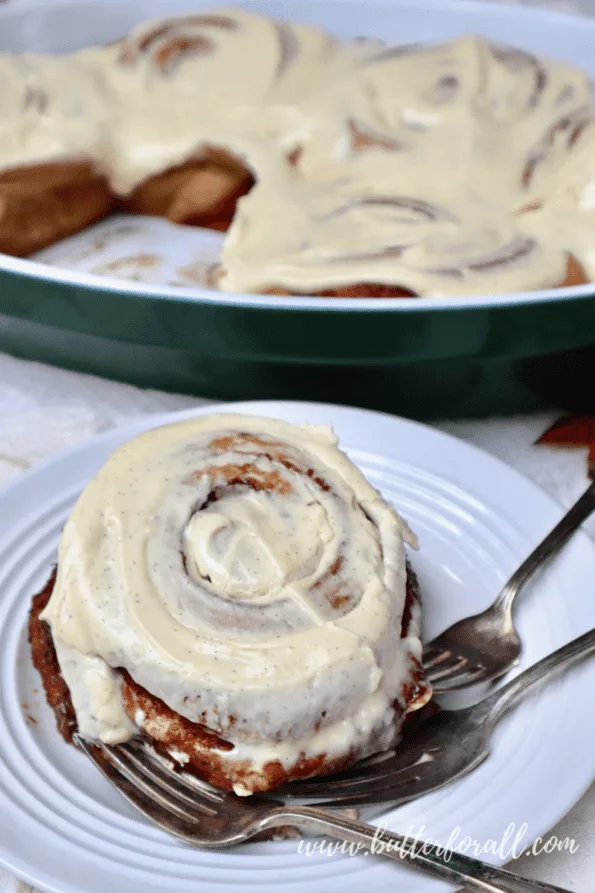 A gooey sourdough cinnamon roll on a plate with three forks.
