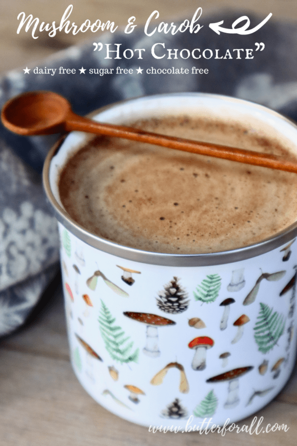 An enamel mug filled with rich looking mushroom hot chocolate and a wooden spoon for stirring.