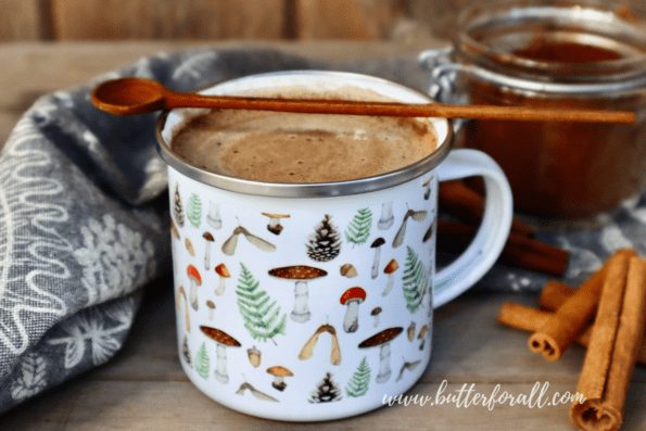 Mushroom hot chocolate in an enamel mug with a jar of chaga mushroom powder and cinnamon sticks nearby.