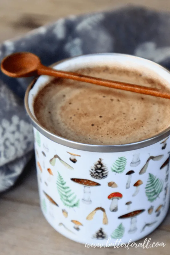 Smooth and swirly mushroom hot chocolate in an enamel mug with wooden spoon.