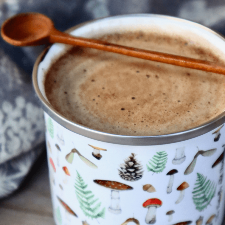 Smooth and swirly mushroom hot chocolate in an enamel mug with wooden spoon.