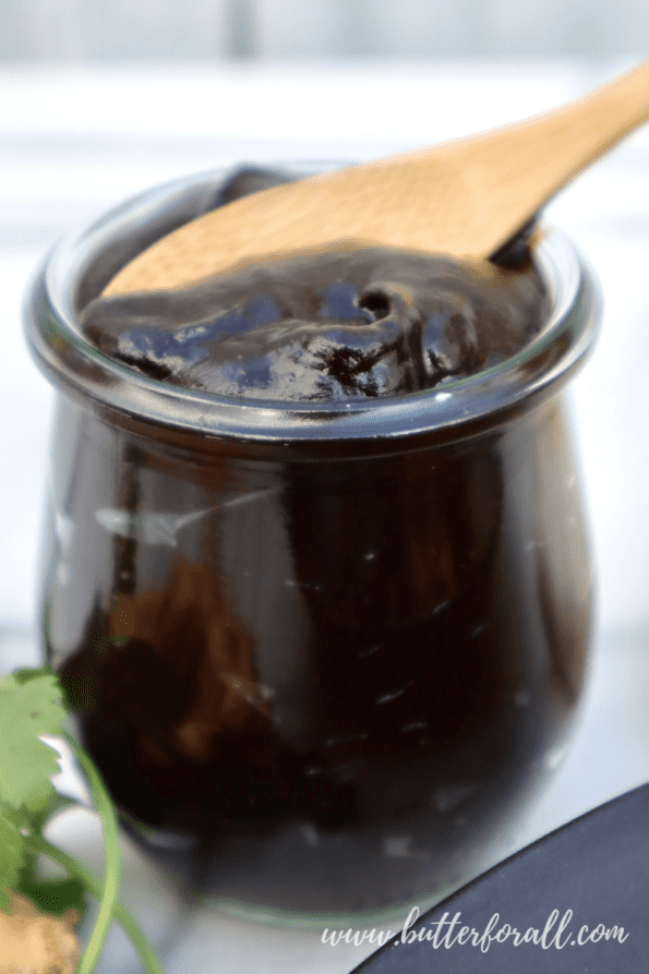 A jar of thick shiny black garlic plum sauce with a wooden spoon. 