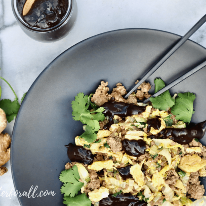 A beautiful shallow black bowl with moo shu beef, shiny black garlic plum sauce, and black chopsticks.