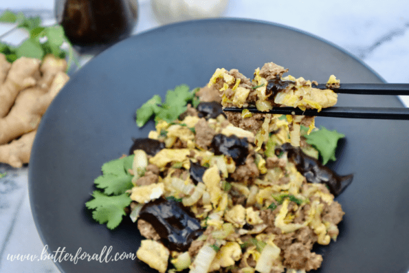 A bite of moo shu beef between two chopsticks.