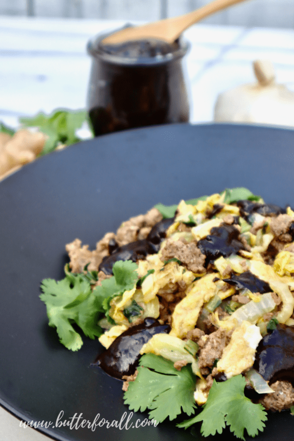 Moo shu beef with cabbage, bok choy, scrambled eggs, and plum sauce in a large shallow black bowl. 