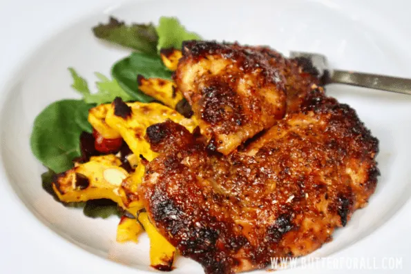 A white plate with roasted honey mustard chicken thighs, delicata squash, and a small green salad. 