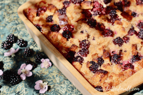 A ceramic pan of fresh baked bread pudding studded with jammy blackberries. 