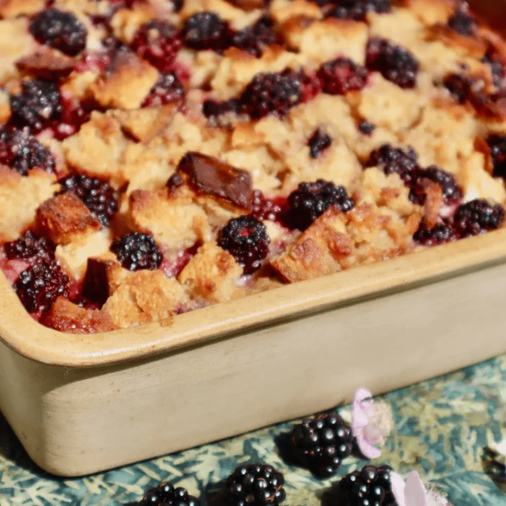 A ceramic pan filled with golden-brown blackberry sourdough bread pudding.