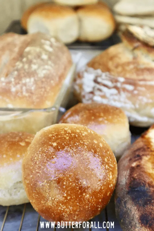 Shiny brown sourdough buns in the forefront with other baked goods surrounding them. 