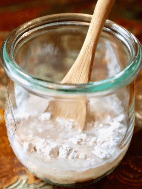 A small jar with flour, dehydrated starter, water, and a small spoon.