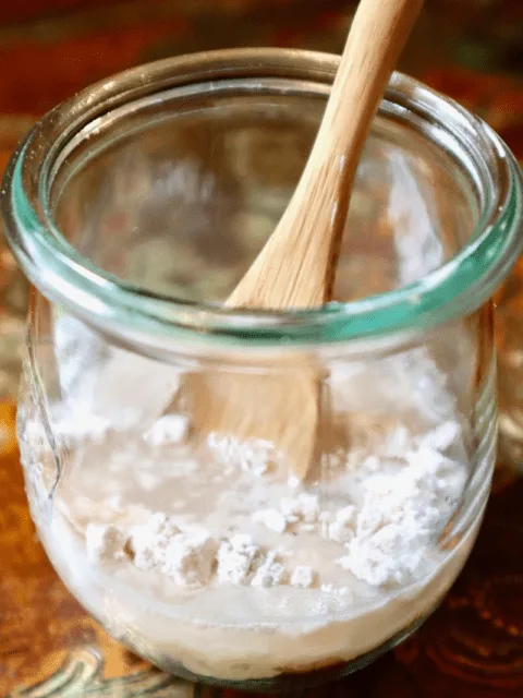A small jar with flour, dehydrated starter, water, and a small spoon.