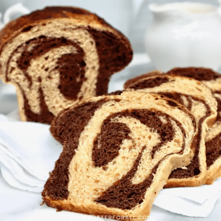 Slices of sourdough Dutch chocolate swirl bread in the foreground with a set of white porcelain cream and sugar containers in the background.