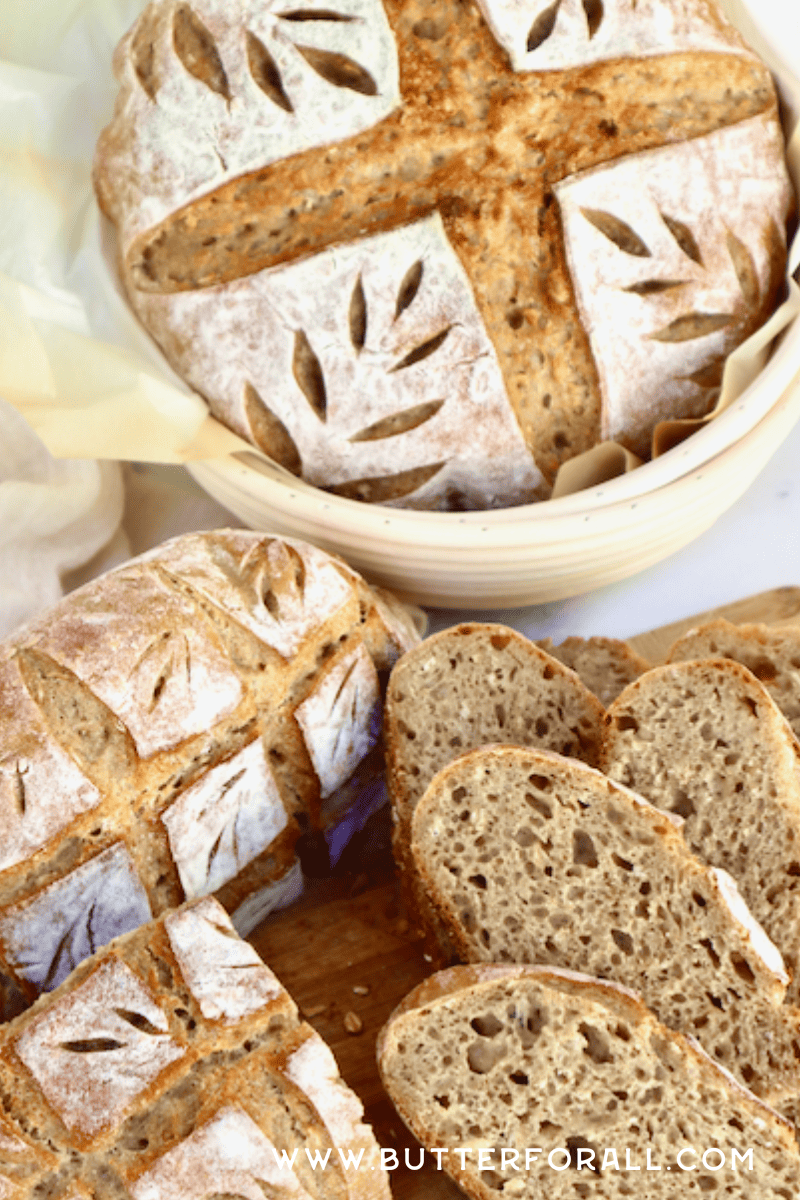 Decorative bread resting in a banneton and surrounded by slices of hearty sourdough.