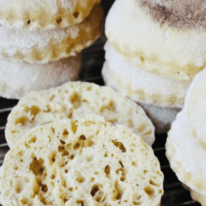 A big stack of freshly cooked einkorn sourdough English muffins. One in the front has been cut open to expose its nooks and crannies.