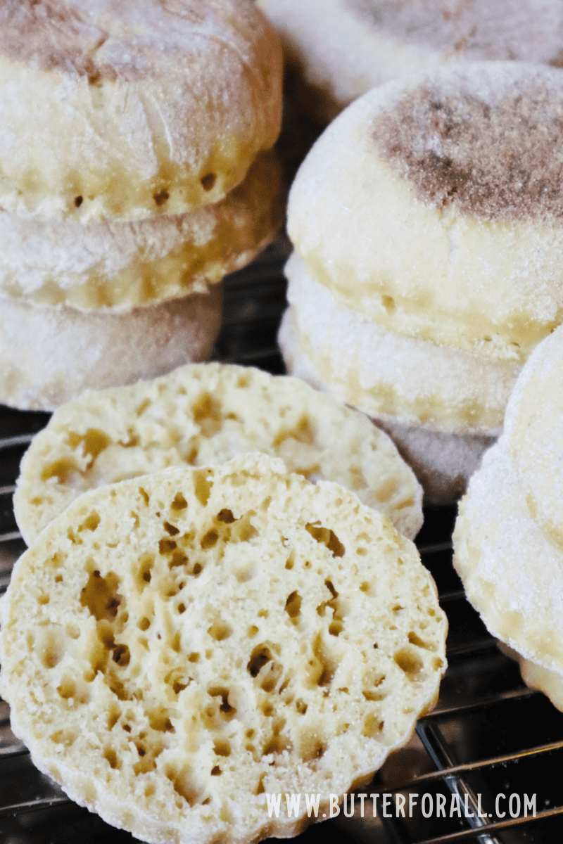 A big stack of freshly cooked einkorn sourdough English muffins. One in the front has been cut open to expose its nooks and crannies.
